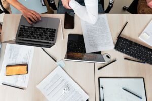 Overhead shot of office desk with laptops, documents, and tech gadgets during a business meeting.