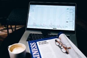 A modern business workspace featuring a laptop showing stock data next to a business magazine and coffee.