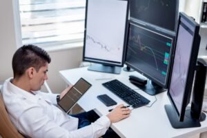 Business professional analyzing financial charts on monitors and tablet in modern office workspace.